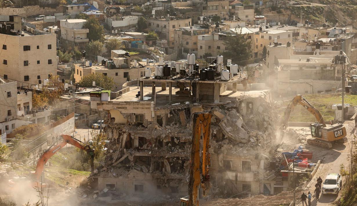 Diketahui, bangunan yang dirobohkan itu terletak di area Silwan, dekat Kota Tua, Yerusalem, yang terdiri atas belasan gedung apartemen yang dihuni sekitar 100 orang, kebanyakan perempuan, anak-anak, dan warga lanjut usia (lansia). Tampak dalam foto, ekskavator merobohkan sebuah bangunan yang dibangun tanpa izin di daerah Wadi Qaddum dekat lingkungan Silwan di Yerusalem timur pada Senin 22 Desember 2025. (Ahmad GHARABLI/AFP)
