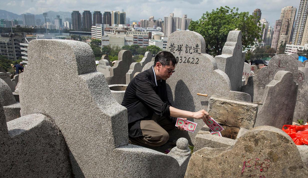 Seorang pria membakar uang kertas di makam seorang kerabat selama festival Qingming di pemakaman di Hong Kong (5/4). Biasanya warga cenderung membuat persembahan untuk keluarga atau kerabat mereka agar tetap nyaman di akhirat. (AFP Photo/Isaac Lawrence)