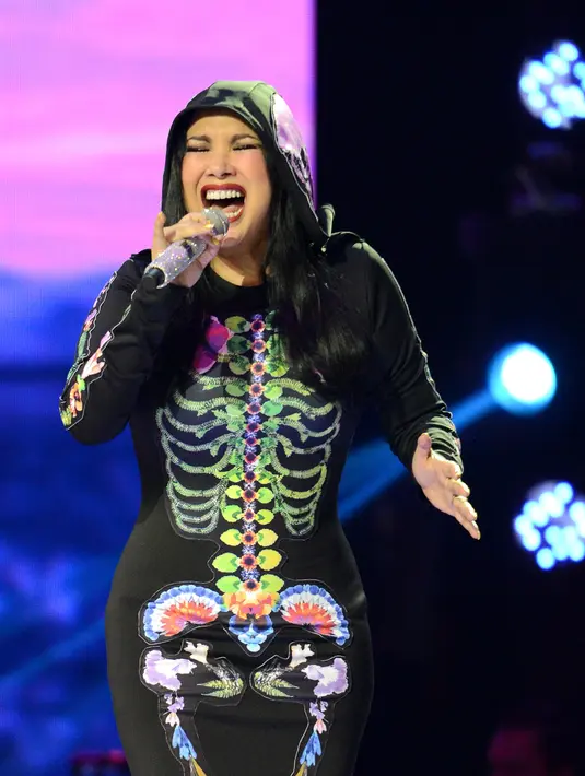 Berbeda dengan gaun sebelumnya, Titi DJ dengan baju bewarna hitam dan aksen tulang tengkorak yang bewarna-warni mampu mencuri perhatian warga net saat bernyanyi di acara Indonesia Idol pada tahun 2014 silam. (Kapanlagi/Bambang E Ros)