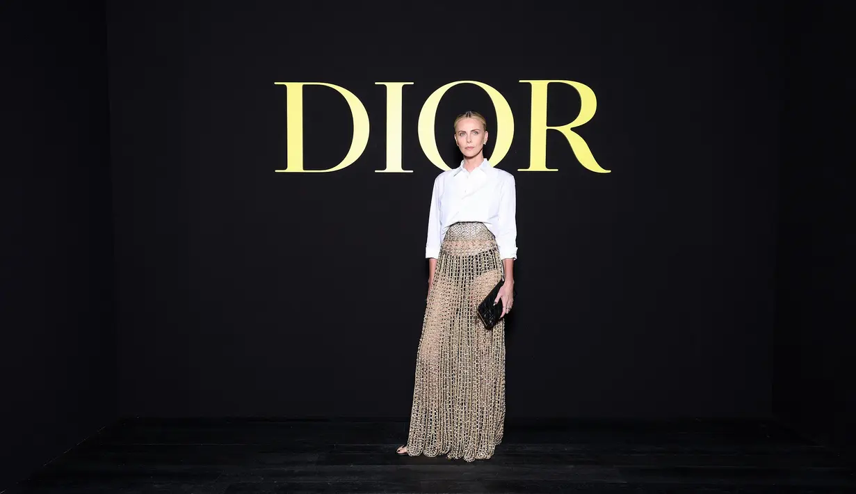 Charlize Theron mengenakan kemeja katun putih Dior di atas rok panjang Dior Haute Couture SS24 yang disulam dengan passementerie dalam kepang, jahitan bourdon, dan simpul emas mengilap. Dia juga mengenakan clutch, sepatu, dan perhiasan dari Dior. [Dior]