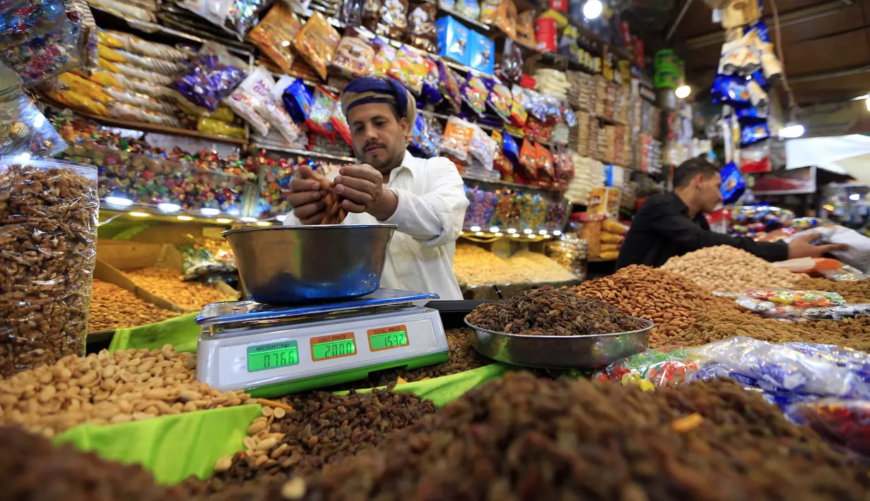 Pedagang buah dan kacang kering menimbang segenggam almond di sebuah toko di Sanaa, Yaman, Rabu (20/5/2020). Umat muslim seluruh dunia bersiap menyambut Idul Fitri yang sekaligus menandai berakhirnya bulan suci Ramadan. (Mohammed HUWAIS/AFP)