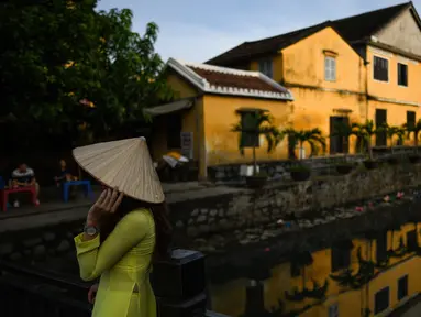 Gambar pada 14 September 2019 menunjukkan seorang turis mengenakan pakaian tradisional Vietnam ketika berpose di kota tua Hoi An. Kota Tua Hoi An merupakan destinasi wisata yang cukup populer di Vietnam, didukung oleh statusnya sebagai salah satu Unesco World Heritage Site. (Manan VATSYAYANA/AFP)
