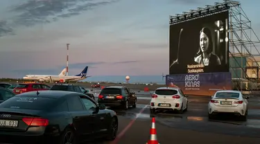 Orang-orang duduk di mobil mereka saat menonton film di bioskop drive-in di area apron bandara kota Vilnius, Lithuania, 29 April 2020. Untuk pertama kalinya dalam sejarah bandara Vilnius mengadakan bioskop drive-in yang beroperasi di tempat pesawat lepas landas dan mendarat. (AP/Mindaugas Kulbis)