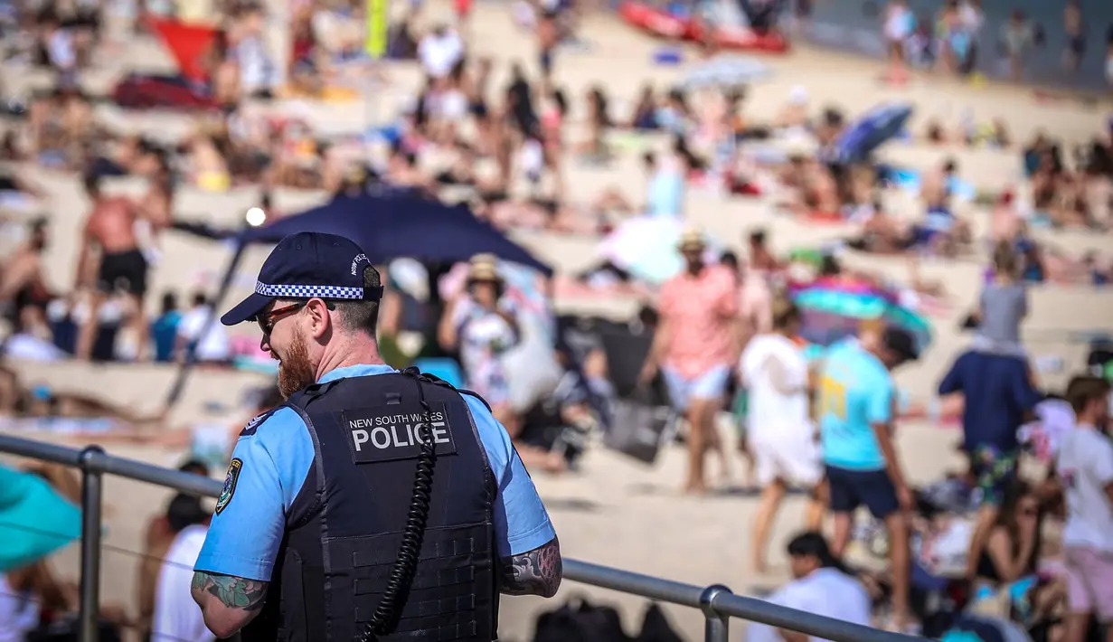 Seorang polisi berpatroli saat orang-orang mengunjungi pantai Bondi di Sydney, Australia pada 5 Oktober 2020. Pengunjung ramai berjemur dan bermain di pantai dan berenang di laut saat pandemi Covid-19 masih berlangsung.  (Photo by DAVID GRAY / AFP)