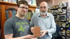 Richard Sprent, pemilik toko buku bekas (kiri) memperlihatkan sebuah buku berusia 200 tahun yang diduga berasal dari jaman Perang Napoleon di toko buku miliknya, di Hobart, ibu kota negara bagian Tasmania, Australia, Selasa (10/5). (STR/AFP)