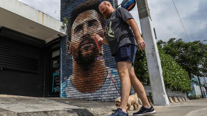 Pejalan kaki melintasi mural wajah Lionel Messi yang berada di salah satu jalan di Miami, Amerika Serikat. Messi memutuskan untuk bergabung dengan klub MLS, Inter Miami, pada Rabu (7/6/2023). (AFP/Giorgio Viera)