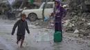 Rata-rata anak-anak di Gaza hanya mendapatkan 1,5 hingga 2 liter air per hari, jauh di bawah kebutuhan dasar manusia. Tampak dalam foto, seorang anak laki-laki tanpa sepatu berjalan di bawah hujan sambil membawa jerigen plastik berisi air di kawasan Sheikh Radwan, Kota Gaza, pada Jumat 14 November 2025. (AP Photo/Jehad Alshrafi)