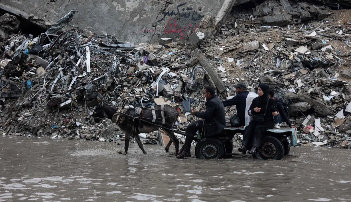 Data Kementerian Kesehatan di Gaza yang dikelola Hamas menyebut, hingga Rabu 26 November 2025, serangan Israel di Gaza telah menewaskan sedikitnya 69.775 orang. Tampak dalam foto, orang-orang menunggangi kereta kuda melewati banjir di kamp darurat yang menampung warga Palestina yang terlantar setelah hujan deras di Kota Gaza pada Selasa 25 November 2025. (Omar AL-QATTAA/AFP)