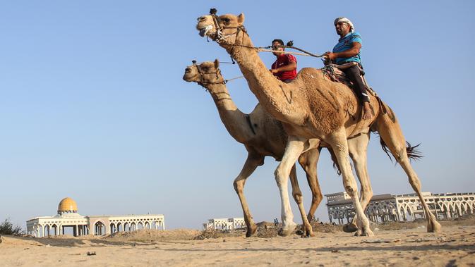 Dua peserta joki bersaing dalam perlombaan balap unta lokal di Rafah, Jalur Gaza selatan (20/10/2019). Balapan unta ini menggunakan lintasan bekas landasan bandara Gaza yang sudah hancur di Rafah, Gaza selatan. (AFP Photo/Said Khatib)