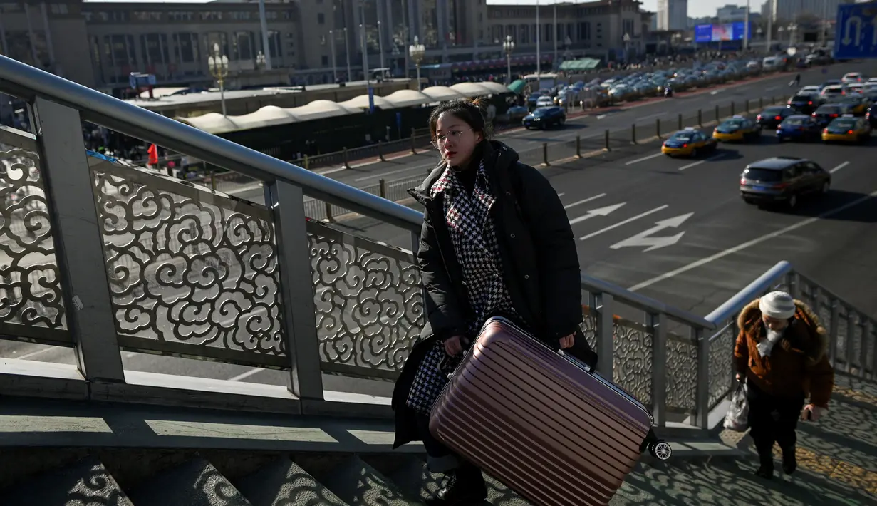 Seorang wanita membawa koper melewati jembatan penyeberangan di luar stasiun kereta api Beijing, Jumat (10/1/2020). Puluhan ribu warga China telah memulai migrasi manusia terbesar di dunia meninggalkan kota-kota besar menuju kampung halaman untuk merayakan Tahun Baru Imlek. (WANG ZHAO/AFP)