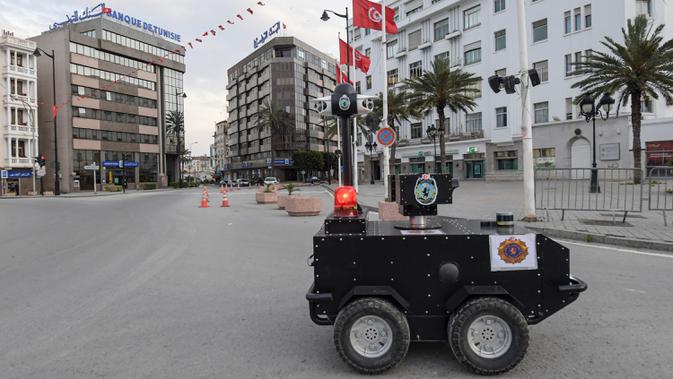 Robot polisi Tunisia berpatroli selama kebijakan penguncian (lockdown) di sepanjang Avenue Habib Bourguiba, pusat ibu kota Tunis, Rabu (1/4/2020). Selain untuk pengawasan dan pemberian sanksi, robot ini juga digunakan memberikan pesan agar warga Tunisia tetap berada di rumah. (FETHI BELAID/AFP)