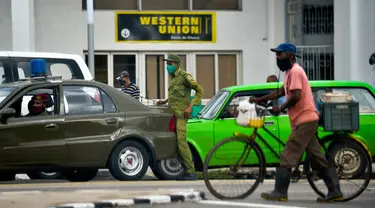 Petugas keamanan terlihat di luar Western Union sebelum penutup kantor di Havana, Kuba, Senin (23/11/2020). Layanan transfer uang terkemuka di dunia itu menutup lebih dari 400 gerainya di Kuba menyusul sanksi ekonomi terbaru yang dikeluarkan Amerika Serikat (AS) terhadap negara itu. (Yamil LAGE/AFP)