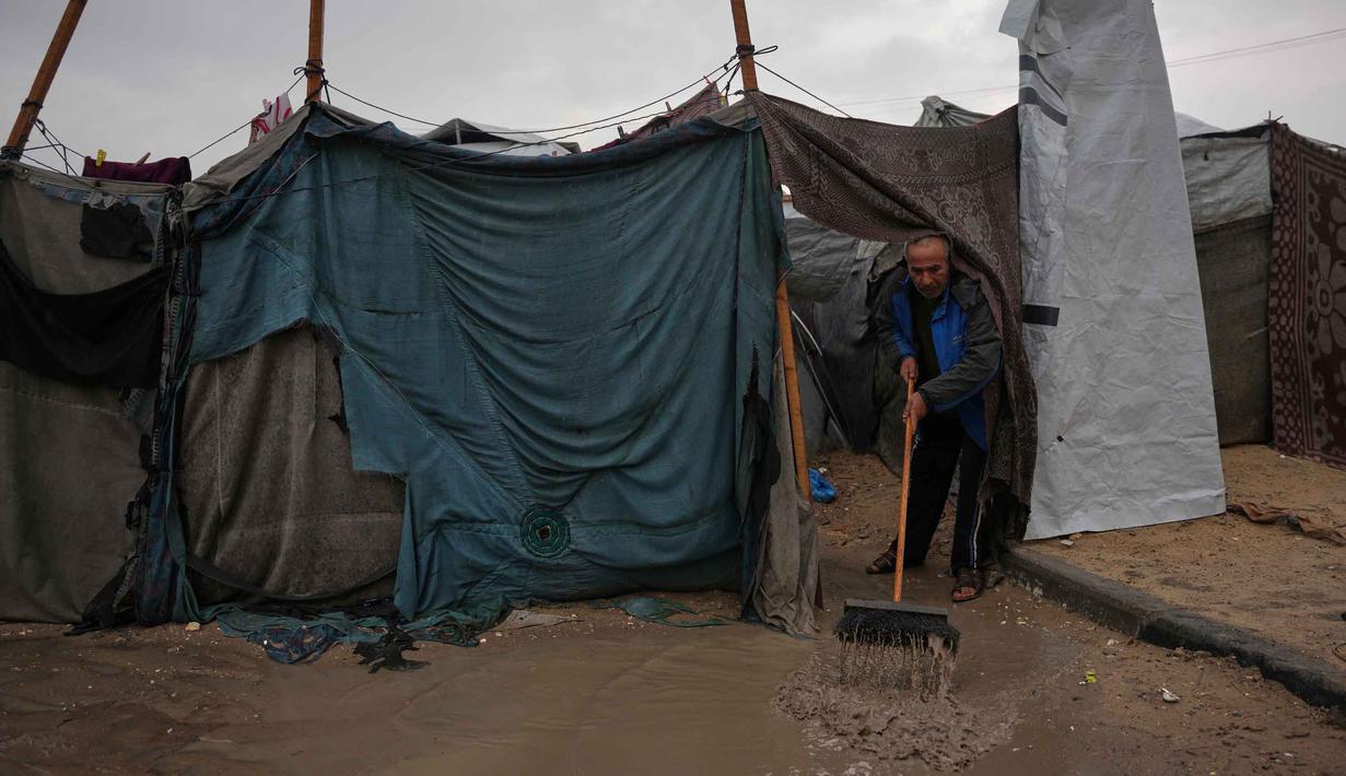 Warga pengungsi harus berjuang untuk tetap kering dan hangat di tengah kondisi yang memburuk. Tampak dalam foto, Hosni Abu Reda membersihkan air dari tendanya di sebuah kamp pengungsi Palestina setelah hujan deras di Khan Younis, Jalur Gaza selatan, Kamis 11 Desember 2025. (AP Photo/Abdel Kareem Hana)
