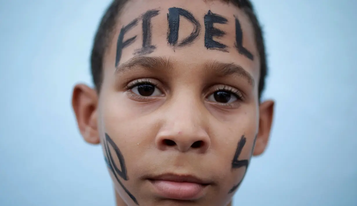 Seorang anak dengan tulisan Fidel di keningnya menunggu mobil yang membawa abu Fidel Castro, lewat di Bayamo, Kuba (3/11). Sebelum dikebumikan, rakyat Kuba memberikan penghormatannya kepada Castro di Jose Marti Memorial. (Reuters/Enrique De La Osa)