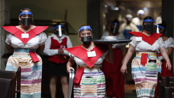 Sejumlah pelayan mengenakan masker dan pelindung wajah untuk mencegah penyebaran virus corona COVID-19 saat mengantarkan makanan di Restoran Sanborns of the Azulejos, Mexico City, Meksiko, Rabu (1/7/2020). (AP Photo/Eduardo Verdugo)
