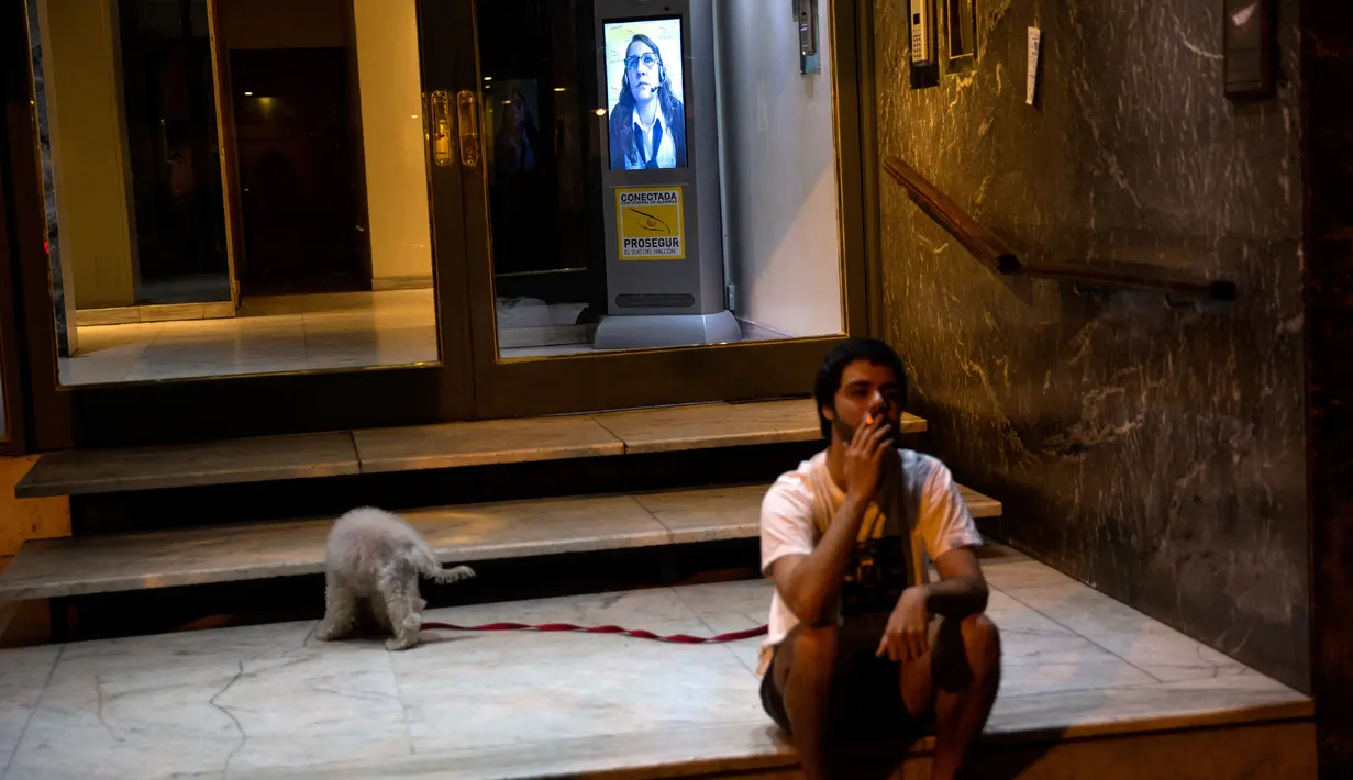 Seorang pria mengisap rokok dekat penjaga keamanan virtual di pintu masuk gedung di Buenos Aires, Argentina, Selasa (24/4). Sistem ini mampu menghemat sekitar 30 persen biaya keamanan. (AP Photo/Rodrigo Abd)