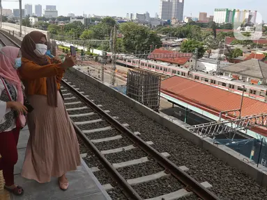 Penumpang berswafoto sambil menunggu kedatangan KRL Commuter Line di Stasiun Manggarai, Jakarta, Minggu (26/9/2021). Jalur layang (elevated track) KRL Bogor Line di Stasiun Manggarai yang terdiri dari empat peron bagi penumpang kereta relasi tujuan Jakarta-Bogor. (Liputan6.com/Herman Zakharia)