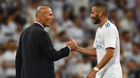 Pelatih Real Madrid, Zinedine Zidane (kiri) bersalaman dengan Karim Benzema merayakan kemenagan atas Barcelona pada Piala Super Spanyol 2017 usai pertandingan melawan Barcelona di stadion Santiago Bernabeu, Spanyol (16/8). (AFP Photo/Gabriel Bouys)