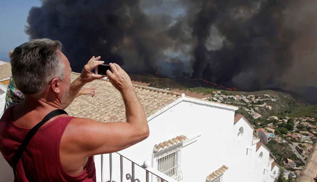Seorang turis mengambil gambar kebakaran hutan di Benitatxell dekat Alicante, Spanyol, Senin (5/9). Sedikitnya 1.000 orang terpaksa diungsikan ke tempat yang lebih aman dari sejumlah vila. (REUTERS / Heino Kalis)