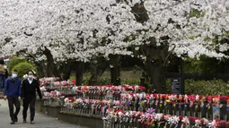 Orang-orang yang memakai masker berjalan-jalan di bawah bunga sakura yang mekar penuh di Kuil Zojoji, Tokyo, Jepang, Selasa (29/3/2022). (AP Photo/Koji Sasahara)