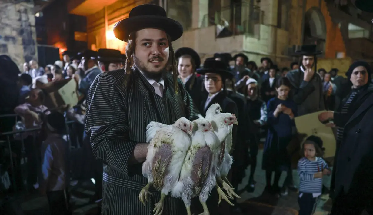 Seorang pria Yahudi ultraortodoks memegang beberapa ekor ayam sebelum melakukan ritual Kapparot di Yerusalem, 12 September 2021. Kapparot adalah ritual transfer dosa ke ayam yang dilakukan sebelum Yom Kippur (Hari Penebusan). (MENAHEM KAHANA/AFP)