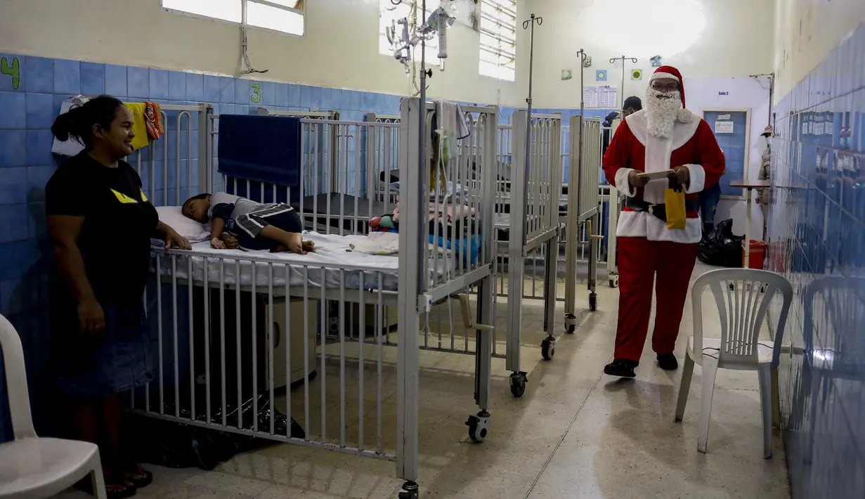 Seorang pria berpakaian seperti Sinterklas berjalan menyusuri lorong untuk mengantarkan hadiah kepada anak-anak yang dirawat di ruang gawat darurat sebuah rumah sakit di lingkungan El Cementerio di Caracas, Venezuela pada 25 Desember 2023. (Pedro Rances Mattey / AFP)