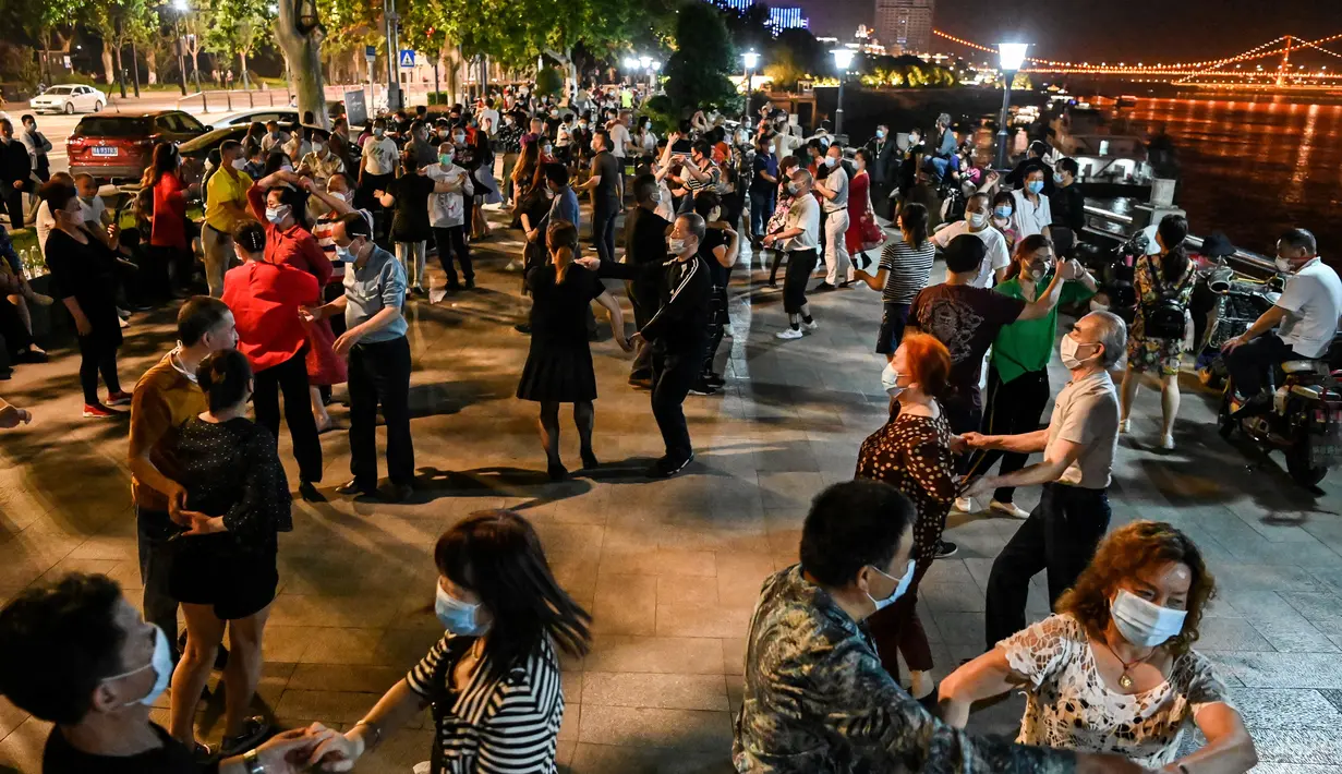 Pasangan mengenakan masker menari di sebuah taman di sebelah Sungai Yangtze, Wuhan, provinsi Hubei tengah China (12/5/2020).  Peningkatan kasus virus corona tersebut memicu kekhawatiran gelombang kedua infeksi. (AFP/Hector Retamal)