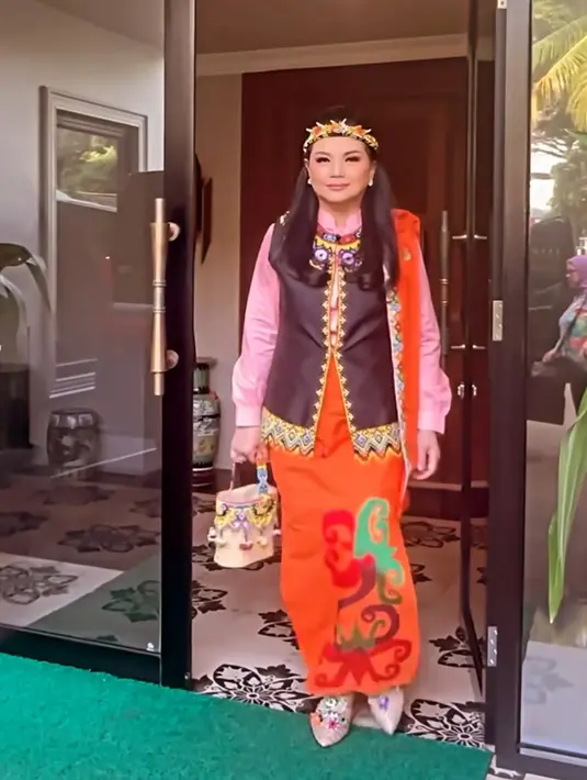Yanti Airlangga tampil dengan baju Dayak dari atasan hitam vest dengan motif bordiran khas Dayak. Dipadukan inner kemeja pink lengan panjang, serta bawahan rok orange bermotif dayak. Lengkap membawa tas handbag dengan beads beraksen Dayak. [@yanti.airlangga]