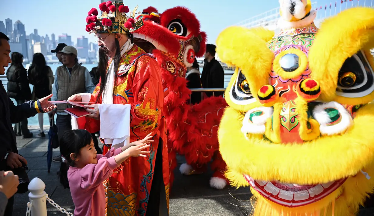 Seorang pria berpakaian seperti Cai Shen Ye atau Dewa Kekayaan Tionghoa membagikan dekorasi tradisional Fai Chun untuk keberuntungan dan kemakmuran di sebuah acara Tahun Baru Imlek di Hong Kong pada tanggal 10 Januari 2025. (Peter PARKS/AFP)