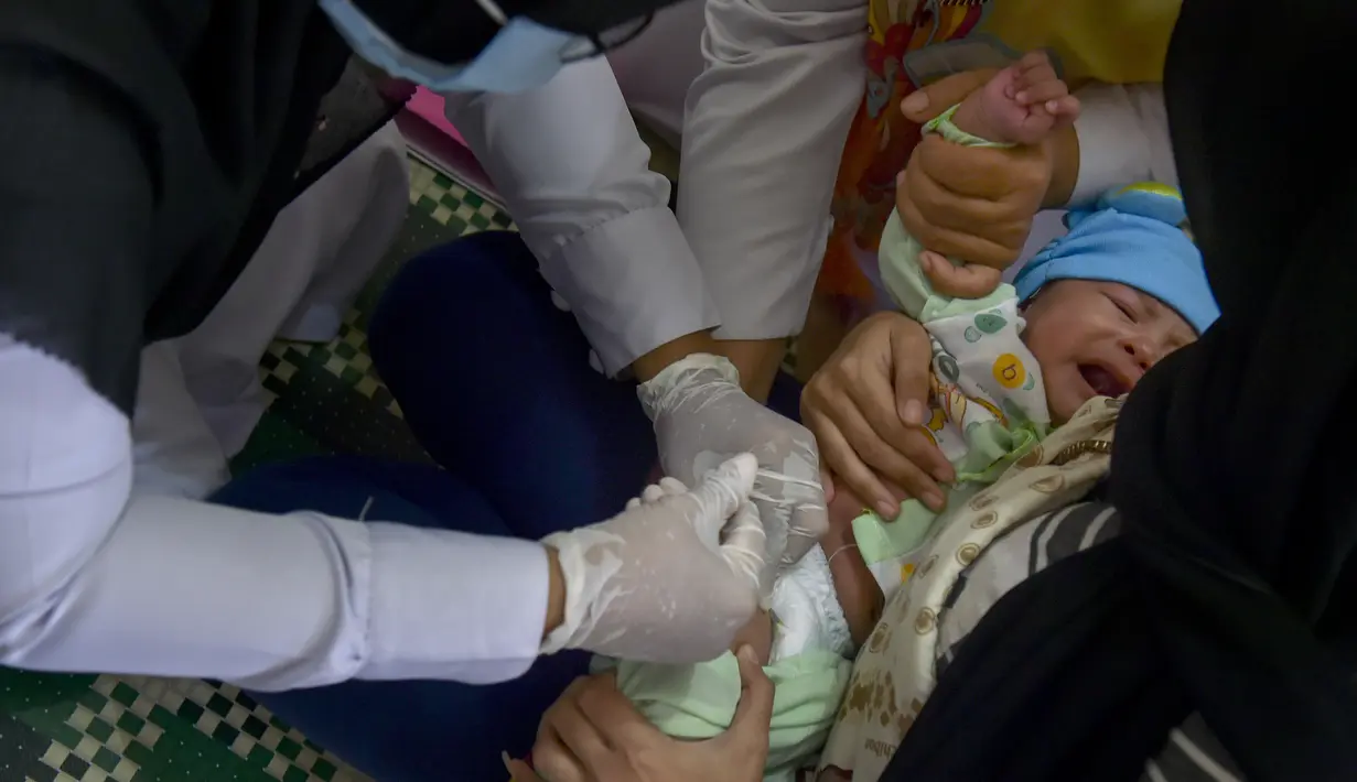 Seorang petugas kesehatan memberikan vaksin campak kepada balita di sebuah posyandu di Banda Aceh, Aceh, Rabu (4/10/2020). Pemberian vaksin polio dan vaksin campak secara gratis yang berlanjut di tengah pandemi COVID-19 bertujuan memperkuat imunitas anak. (CHAIDEER MAHYUDDIN / AFP)