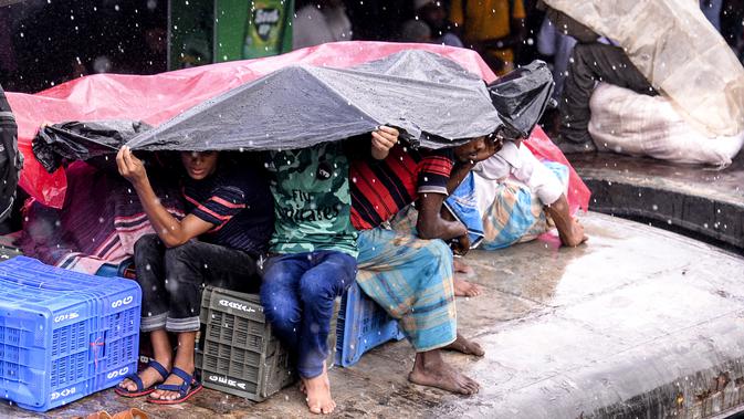 Warga Bangladesh melindungi diri mereka dari hujan saat duduk di atas atap kereta untuk menuju kampung halaman di Dhaka pada 4 Juni 2019. Sebagaimana terjadi di Indonesia, masyarakat Bangladesh pun memiliki tradisi mudik saat Idul Fitri, namun agak membahayakan keselamatan. (MUNIR UZ ZAMAN/AFP)