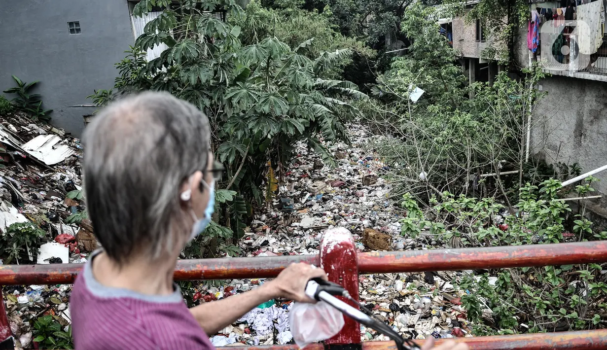 Warga melihat tumpukan sampah di aliran Kali Baru, Jalan Raya Bogor, Cimanggis, Depok, Jawa Barat, Minggu (24/1/2021).  Menumpuknya sampah di perbatasan antara Jakarta dan Depok itu juga diperparah dengan kondisi sungai yang menyempit dan mengalami pedangkalan. (merdeka.com/Iqbal S. Nugroho)