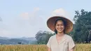 Senyum bahagia tidak bisa disembunyikan Prisia Nasution saat berada di sawah dengan tanaman padi yang terlihat menguning. Dengan memakai caping, ia sangat bahaga berada di antara tanaman padi di sawah. (Liputan6.com/IG/@prisia)