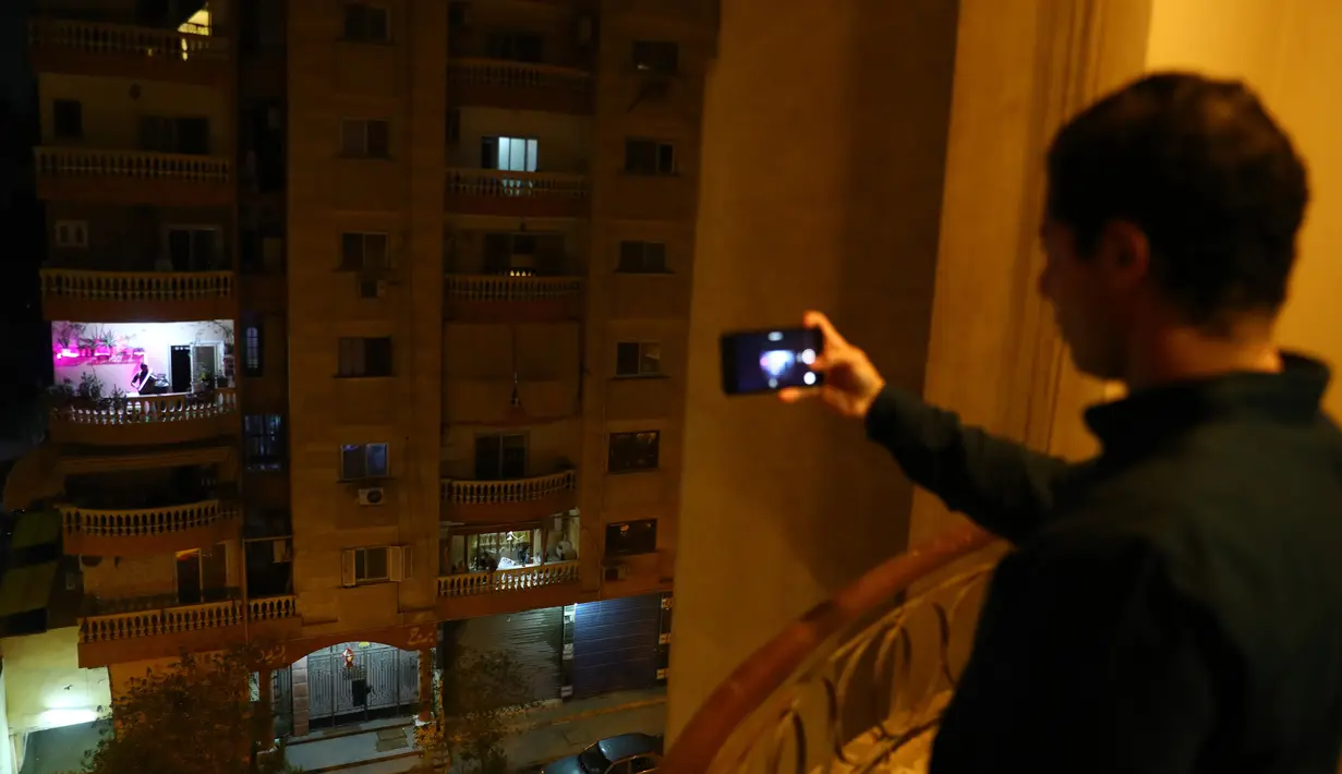 Warga mengabadikan foto konser biola yang digelar dari atas balkon di Kairo, pada 31 Maret 2020. Setiap malam, pemain biola asal Mesir Mohammed Adel menampilkan konser dari balkonnya untuk menghibur para tetangga selama jam malam nasional yang diberlakukan akibat COVID-19. (Xinhua/Ahmed Gomaa)