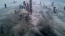 Pemandangan ini menciptakan ilusi kota di atas awan, dengan bagian atas gedung menembus kabut tebal. Tampak foto udara memperlihatkan gedung pencakar langit yang tertutup kabut pagi di Kota Kuwait pada Minggu 9 November 2025. (YASSER AL-ZAYYAT/AFP)