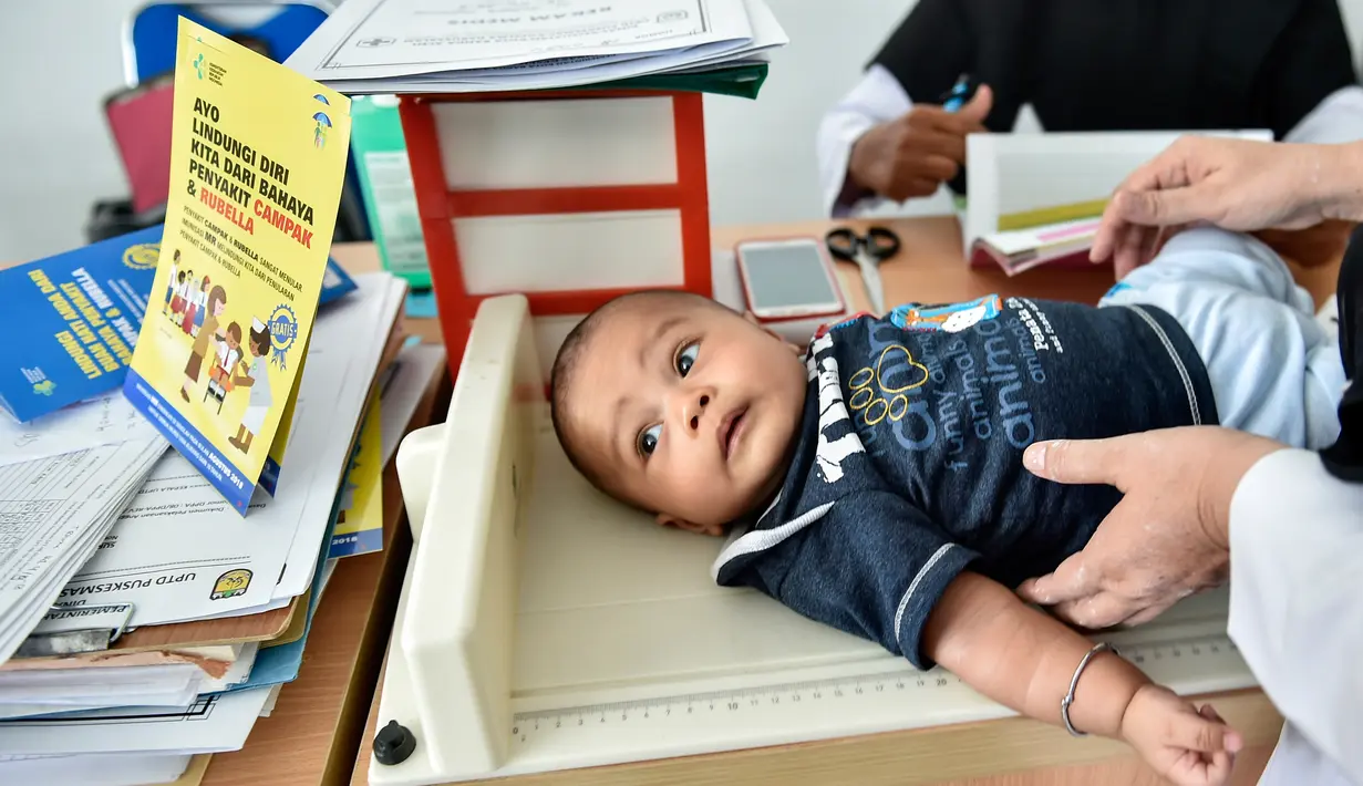Petugas memeriksa bayi sebelum menyuntikan Vaksin Campak dan Rubella (MR) saat dilakukan imunisasi di sebuah puskesmas, Banda Aceh, Rabu (19/9). Pemprov Aceh akhirnya membolehkan pelaksanaan vaksinasi MR yang mengandung enzim babi (CHAIDEER MAHYUDDIN/AFP)