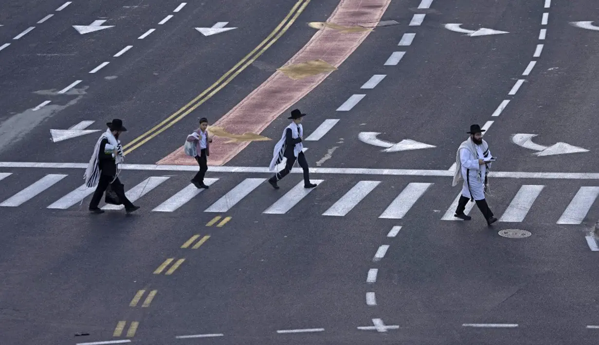 Orang-orang Yahudi ultraortodoks melintasi jalan raya bebas mobil saat warga Israel merayakan puasa Yom Kippur dan tidak mengemudi, Yerusalem, 4 Oktober 2022. Yom Kippur yang juga dikenal sebagai Hari Penebusan adalah salah satu hari libur terpenting Yahudi di mana orang Israel menjalankan puasa, refleksi, dan doa selama 25 jam. (MENAHEM KAHANA/AFP)