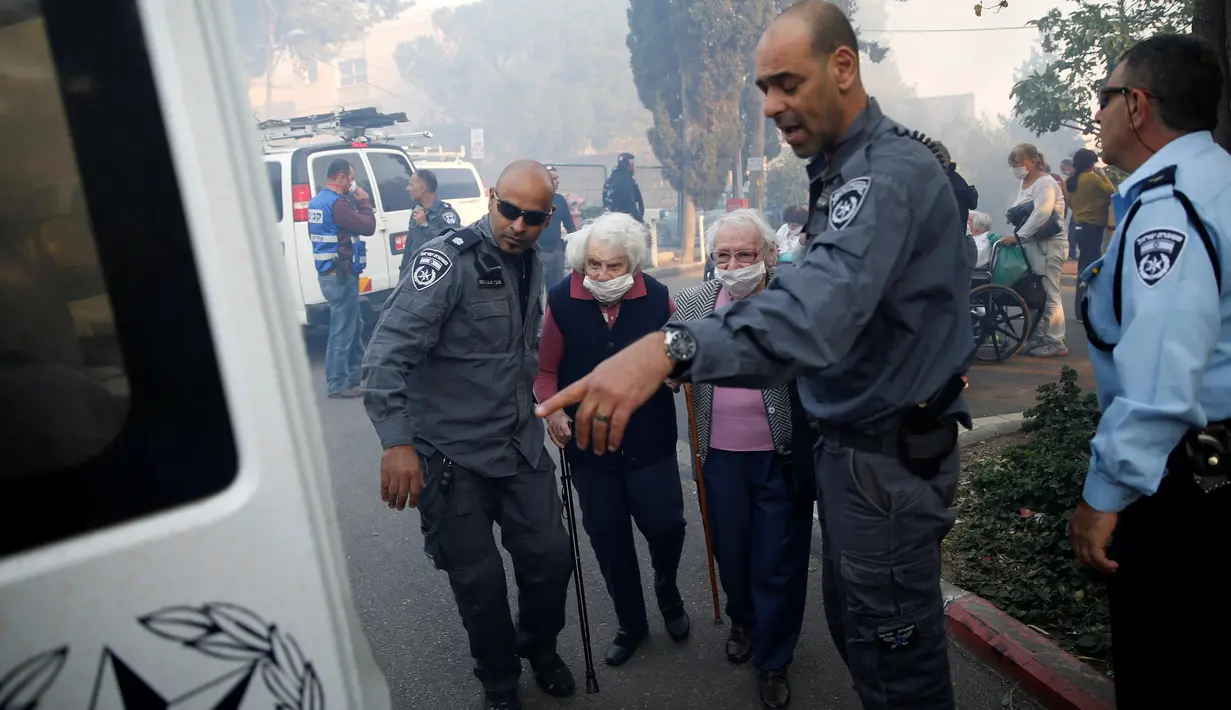 Petugas polisi membantu mengevakuasi sejumlah lansia di kota utara Israel, Haifa, Kamis (24/11). Sekitar 80 ribu warga dievakuasi dan terpaksa meninggalkan rumah mereka akibat kebakaran hutan yang melanda seluruh wilayah tersebut. (REUTERS/Baz Ratner)