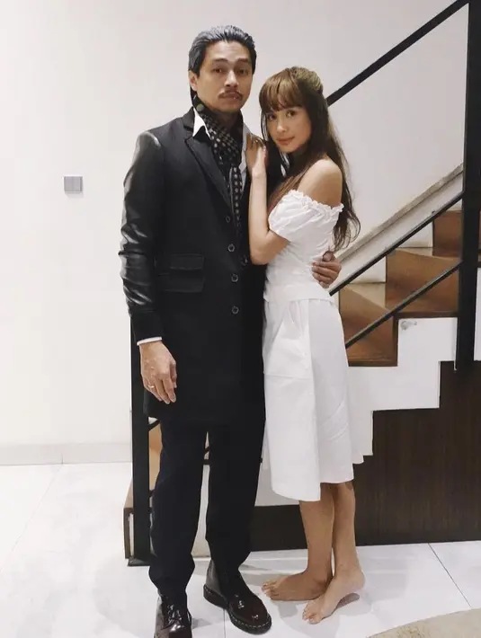 Mikha Tambayong mengenakan atasan off shoulder putih yang serasi dengan midi skirt, sedangkan Deva mengenakan coat dan celana hitam. Keduanya cosplay menjadi Brunette Kim dan The Inventor. @mikhatambayong.