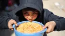 Patut dicatat, terdapat sekitar 1,9 juta dari total populasi 2,4 juta warga Gaza yang bertahan hidup di lokasi-lokasi pengungsian, banyak di antaranya tinggal di tenda darurat setelah rumah mereka hancur akibat konflik berkepanjangan antara Israel dan Hamas. Tampak dalam foto, seorang anak laki-laki Palestina yang mengungsi makan dari mangkuk setelah menerima makanan dari dapur amal di kamp pengungsi Nuseirat, Jalur Gaza Tengah pada 13 April 2026. (Eyad Baba/AFP)