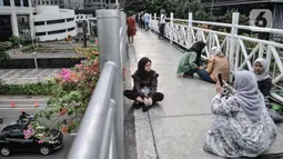 Warga berfoto dengan latar belakang gedung perkantoran di jembatan penyeberangan orang (JPO) tanpa atap di kawasan Sudirman, Jakarta, Minggu (4/4/2021). JPO tanpa atap masih menjadi wisata alternatif warga ibu kota menghabiskan waktu akhir pekan untuk berfoto-foto. (merdeka.com/Iqbal S Nugorho)