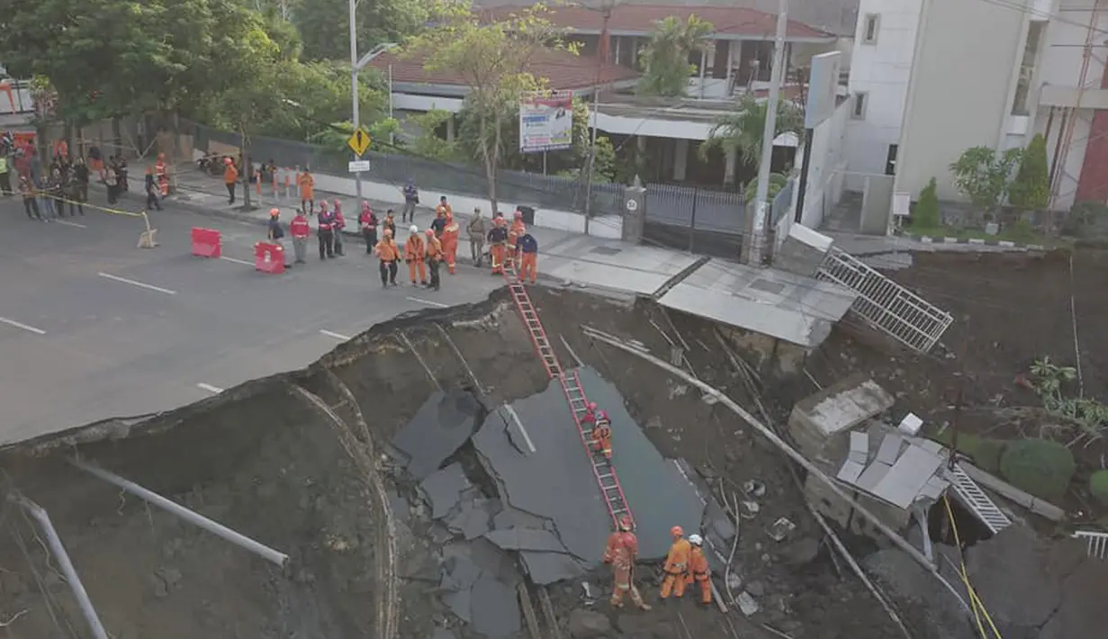 Petugas pemadam kebakaran memeriksa kondisi tanah amblas di Jalan Raya Gubeng, Surabaya, Rabu (19/12). Salah satu akses utama di Kota Surabaya itu amblas diduga karena proyek pembangunan gedung di sekitar lokasi (Liputan6.com/Pool/FB Dishub Kota Surabaya)