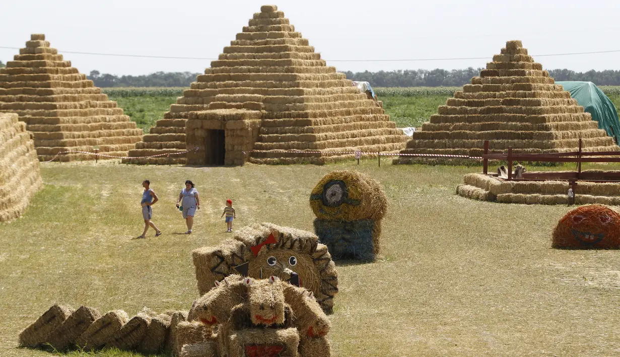 Pengunjung berjalan di sekitar replika Piramida Giza yang terbuat dari jerami di permukiman Krasnoye, Rusia, Rabu (19/7). Piramida unik itu salah satu bangunan yang menghiasi taman jerami di wilayah pertanian Ponomaryovo. (REUTERS/Eduard Korniyenkov)