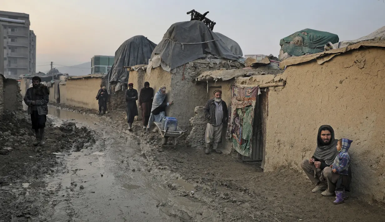 Seorang pria Afghanistan duduk di dinding ketika yang lain berjalan melalui jalan berlumpur di sebuah kamp di Kabul, Afghanistan (27/11/2019). Puluhan ribu warga Afghanistan yang terlantar secara internal tinggal di kamp-kamp, yang kekurangan fasilitas dasar, di Afghanistan. (AP Photo/Altaf Qadri)