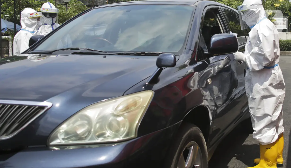 Petugas berpakaian APD lengkap melayani pasien yang secara mandiri melakukan swab test drive thru di halaman parkir rumah sakit di Jakarta, Rabu (12/5/2020). Swab test drive thru dilakukan untuk mendeteksi dan mencegah penyebaran virus corona COVID-19. (Liputan6.com/Johan Tallo)