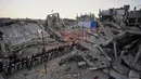 Kelangkaan bahan pokok dan harga yang melambung tinggi membuat banyak warga tidak mampu membeli kebutuhan untuk sahur dan berbuka. Tampak dalam foto, warga Palestina duduk di meja panjang di tengah reruntuhan bangunan yang hancur untuk berbuka puasa bersama, selama bulan suci Ramadan di Khan Younis, Jalur Gaza, Kamis 19 Februari 2026. (AP Photo/Abdel Kareem Hana)