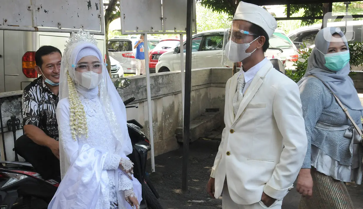 Sepasang pengantin yang menggunakan masker seusai prosesi pernikahan di KUA Pamulang, Tangerang Selatan, Selasa (22/2/2022). Sebanyak 10 pasangan menjalankan akad nikah di KUA Pamulang pada hari ini yang dianggap memiliki tanggal cantik. (merdeka.com/Arie Basuki)