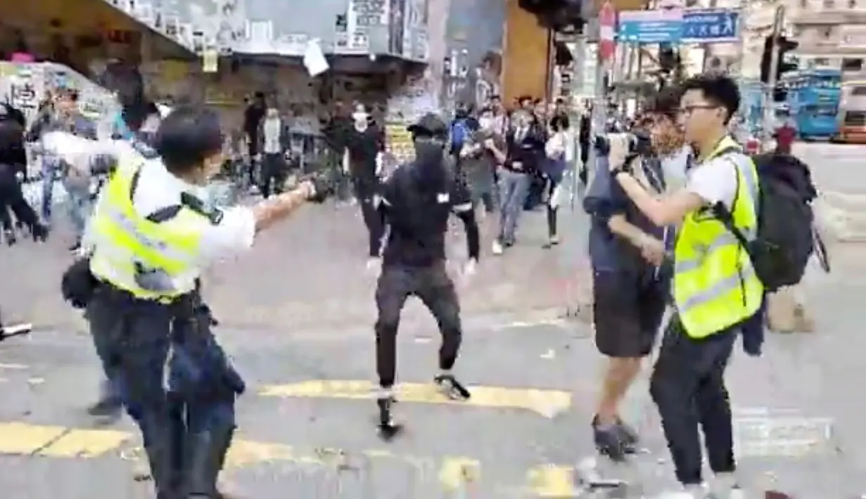 Polisi (kiri) bersiap untuk menembak seorang demonstran prodemokrasi (tengah) saat terjadi protes di Distrik Sai Wan Ho, Hong Kong, Senin (11/11/2019). Polisi menembak seorang pria bertopeng saat tengah berupaya menahan seorang demonstran. (Cupid Producer via AP)