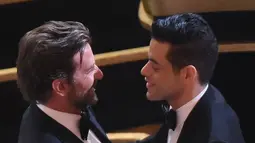 Aktor Bradley Cooper memberi ucapan selamat kepada Rami Malek sebelum menerima penghargaan di atas panggung Oscar 2019, Los Angeles, Minggu (24/2). Rami Malek menyabet Aktor Utama Terbaik di ajang Oscar untuk film Bohemian Rhapsody. (VALERIE MACON / AFP)