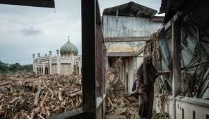 Seorang siswi berjalan di atas bangku untuk menghindari lumpur karena tumpukan pohon tumbang yang tersapu banjir bandang masih berada di Pesantren Darul Mukhlisin dan masjid yang terhubung dengannya di Aceh Tamiang, pada Minggu 14 Desember 2025. Pemandangan memprihatinkan masih terlihat di Pondok Pesantren Darul Mukhlisin, Aceh Tamiang, Minggu (14/12/2025). (Yasuyoshi Chiba/AFP)